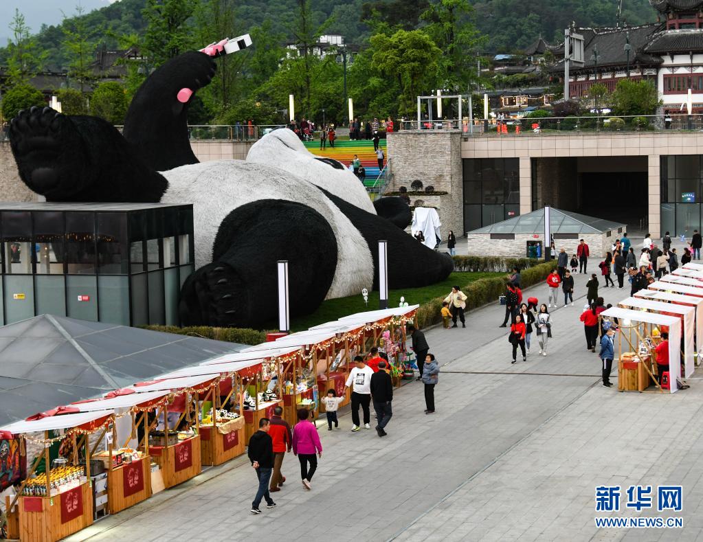 4月7日，在四川省都江堰市仰天窝广场，游客在“自拍熊猫”雕塑旁边的文创集市消费。
